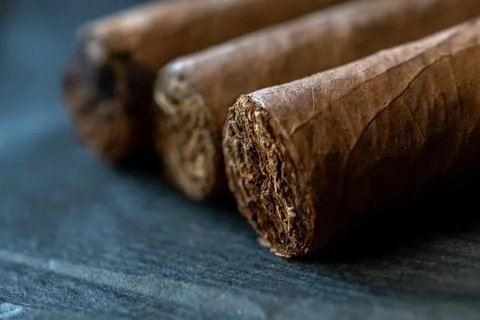 Closeup of three brown cigars arranged diagonally on dark surface Foto stock
