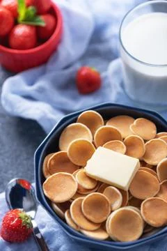 Closeup tiny cereal pancakes with slice of butter, strawberries, glass of mil Stock Photos