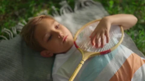 Closeup tired boy lying blanket in summer park examining badminton racket net. Stock Footage 170524128