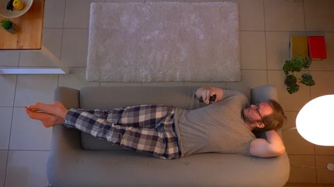 Closeup top shoot of young casually dressed male watching TV lying on the couch Video stock 106939898