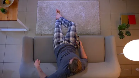 Closeup top shoot of young casually dressed male watching TV while sitting on Video stock 106940724