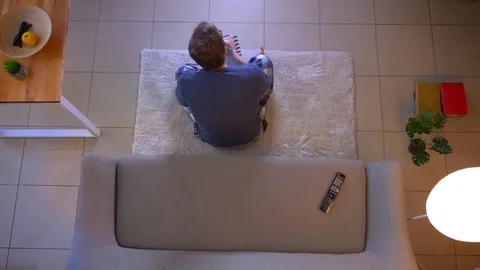 Closeup top shoot of young casually dressed male watching TV sitting on the Video stock 106944765