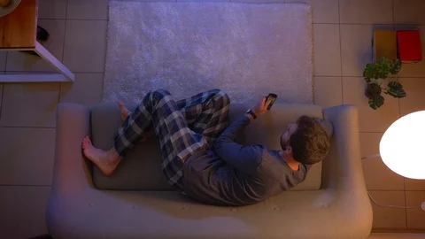 Closeup top shoot of young cute male watching TV lying on the couch indoors at Stock-Footage 106953470