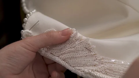 A closeup top view of woman's hands sewing beaded lace down the wedding dress; Video stock 99048304