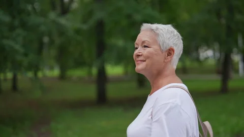Closeup tracking shot of happy elderly 65s female walking through natural park Stock Footage 281371717