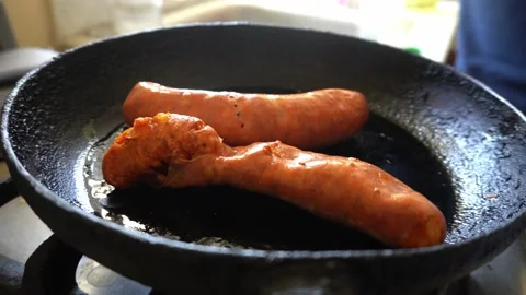 Closeup trying to remove the plastic from a sausage by frying it in the pan with Stockbeeldmateriaal 170015756