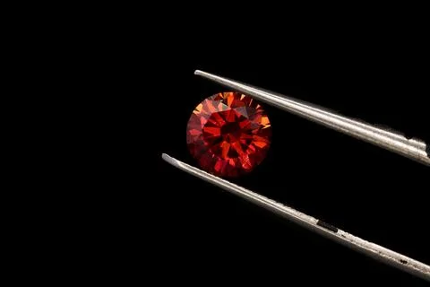 Closeup of tweezers holding a piece of ruby isolated on a black background Stockfoto's