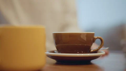 Closeup of two ceramic cups one yellow other brown with saucer on wooden table Stock Footage 346731602