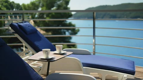 Closeup of two cup of coffee with empty blue deck chairs on the terrace Stock Footage 131112870