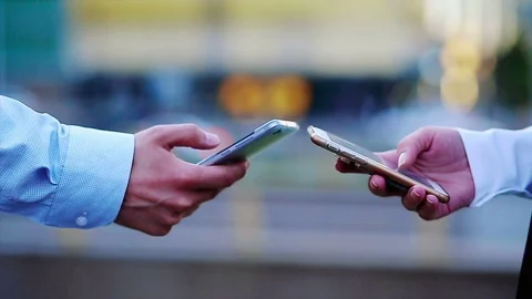 Closeup of two hands using mobile phones with a great cityscape at the Stock Footage 76696235