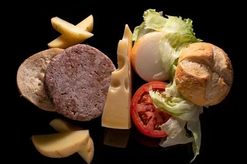 Closeup of uncooked burger, bread, tomato, lettuce, cheese, onion and sliced pot Stock Photos