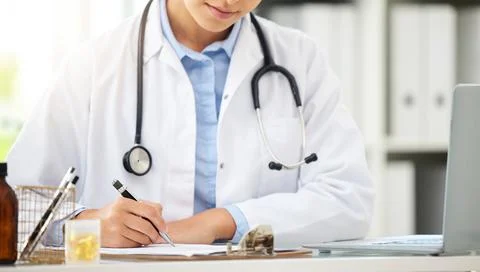 Closeup of an unknown doctor sitting alone in her clinic and writing notes Stock Photos
