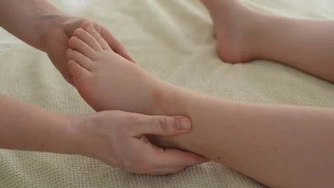 Closeup of unrecognizable doctor doing gymnastics and foot massage to five year Stock Footage 247544211