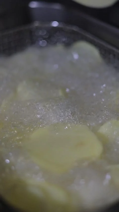 Closeup vertical footage of throwing the raw potato chips in deep boiling oil, Stock Footage 276799980