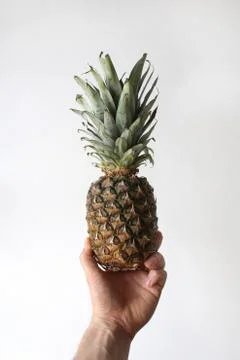 A closeup vertical shot of a person's arm holding a pineapple in hand on a wh Stock Photos