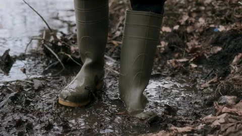 A closeup of vibrant rubber boots stepping through muddy terrain, showcasing the Stock Footage 305407346