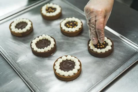 Closeup view of a baker's hand adding golden sprinkles to the chocolate cakes at Stock Photos