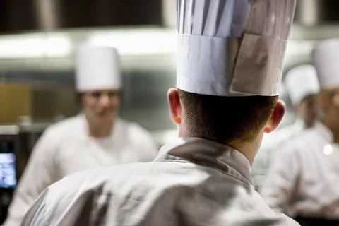 A closeup view from behind of a chef  wearing a toque hat in a commercial Stock Photos