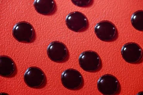 Closeup view of black fluid drops on a textured red background Stock Photos