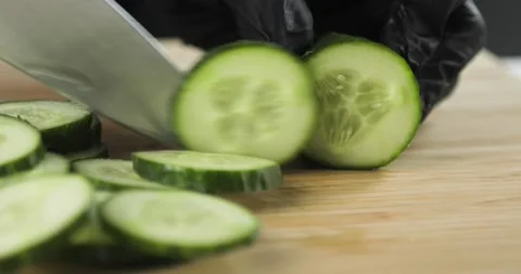 Closeup view of chef's hands in black gloves cutting fresh cucumber into slices. Stock Footage 147432598