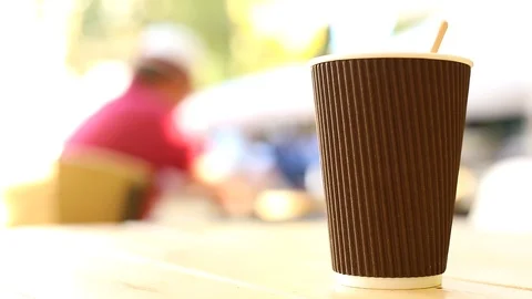 Closeup view of coffee cup on table outside with sunny city on blurred backgroun Vidéo 117409025