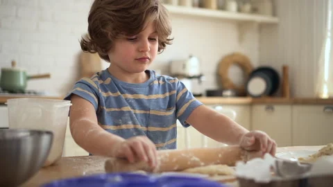 Closeup view of cute boy rolling out dough and sitting at table in home kitchen Stock Footage 161121691