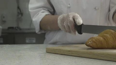 Closeup view of a factory worker wearing gloves cutting a croissant in two, f Stock Footage 132973010