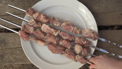 Closeup view of female hands puts raw meat on a skewer on a dish. Stockbeeldmateriaal 129316539