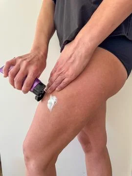 Closeup view of a hand applying white moisturizing cream to the thigh, showin 스톡 사진