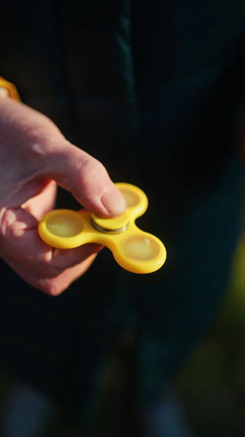 A CloseUp View of a Hand Skillfully Spinning a Bright Yellow Fidget Spinner Stock Footage 308335591
