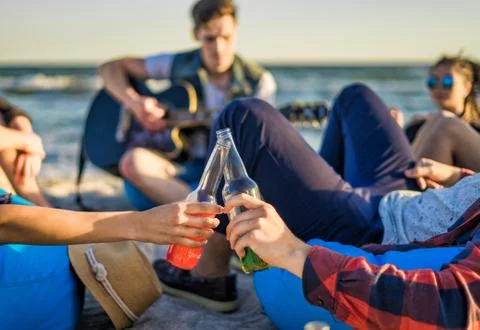 Closeup view of hands clinking glasses of beer bottles on the beach Stock Photos
