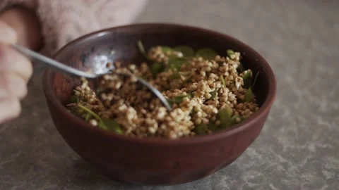 Closeup view of hands mixing sprouted green buckwheat with spinach in clay bowl 動画素材 152043551