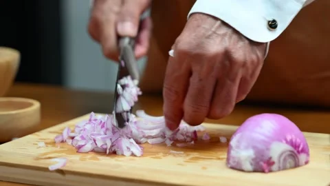 Closeup view of hands slicing red onion on wooden board using a sharp knife.. Video stock 312978813