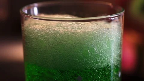 Closeup view how foam disappears in green estragon lemonade in the water glass. Stock Footage 114235603