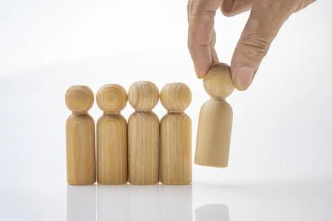 Closeup view of a human hand picking up one of a row of wooden figures Foto stock