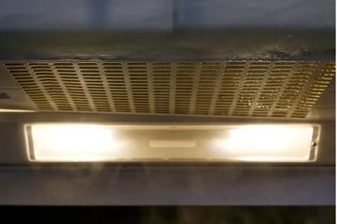 A closeup view of a kitchen range hood with a light on, showing steam rising  Stock Photos