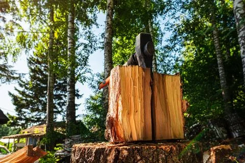 Closeup view of large split log with axe stuck in wooden stump under summer sun Stock Photos