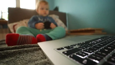 Closeup view of lighted laptop keyboard with unfocused little baby boy on Video stock 98562628