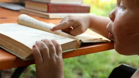 Closeup view of little boy tapping finger in open book with interested face Vidéo 114129536