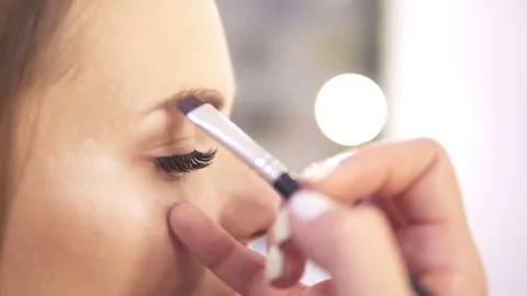 Closeup view of an makeup artist brushing eyebrows of a fashion model while Stock Footage
