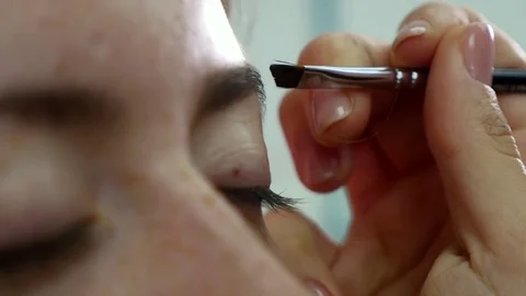 Closeup view of the makeup artist's hands using brush to paint eyebrows for a Stock Footage 82303755