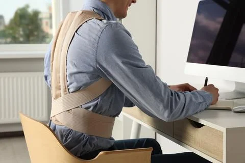 Closeup view of man with orthopedic corset working on computer in room Stock Photos