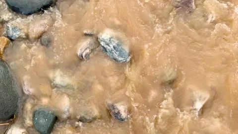Closeup view of a muddy stream flowing over smooth rocks with swirling wate.. Stock-Footage 339368886