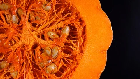 Closeup view of raw pumpkin with seeds rotating on black background in 4K. Видео 86098523