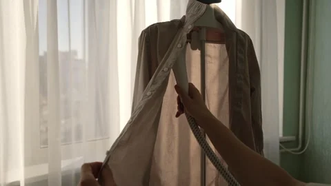 Closeup view from shoulder of unrecognizable person using garment steamer to Stock Footage 304864487