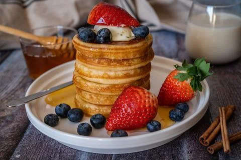 Closeup view of Stack of pancakes with honey stick, strawberry, blue berry an Stock Photos