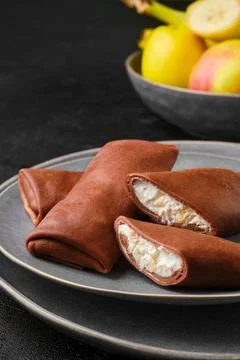 Closeup view of thin chocolate pancakes stuffed with curd, banana and apple Stock Photos