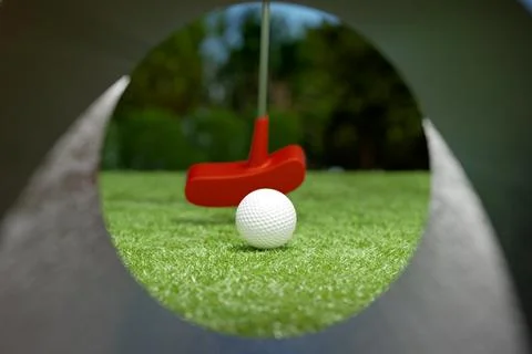A closeup view of a white golf ball rolling towards a red putter Illustrazione stock