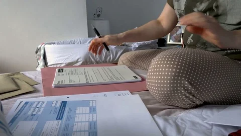 Closeup view of woman in pyjama sorting financial documents on her bed Stock Footage 77875933