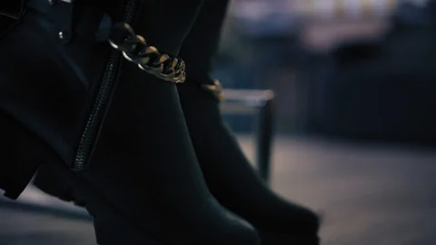 Closeup view on woman's black boots with goldish chains stand on a footrest in Stock Footage 86698341
